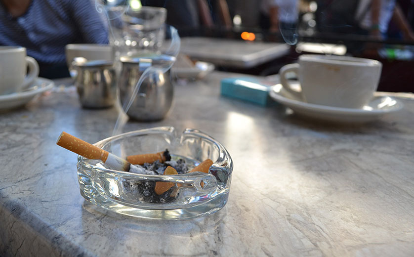 Photo of a lit cigarette in a glass ashtray.