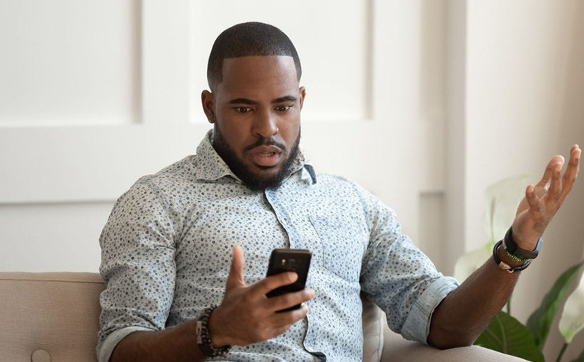 An African American man looks at his phone with a startled look on his face.