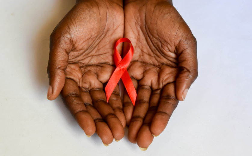 Two brown hands holding a red HIV awareness ribbon