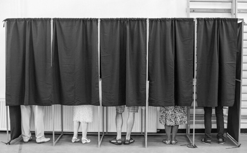 A diverse group of voters in curtained booths; black and white, lower legs visible