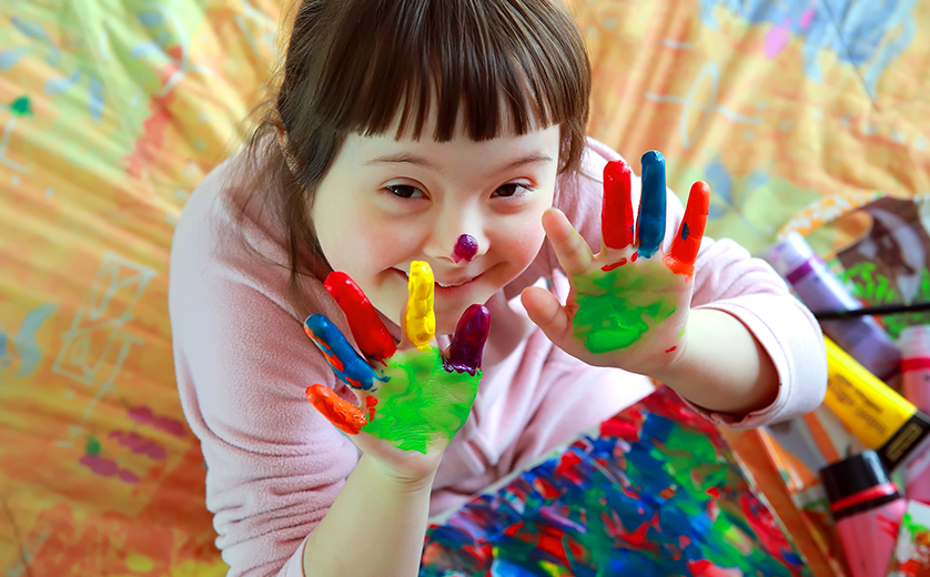 A young girl holds up hands with fingerpaint; colorful