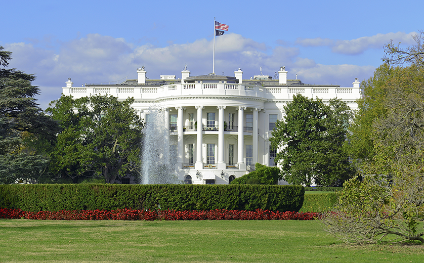 Photo of the White House across green lawn on a sunny day; fountain on the left.